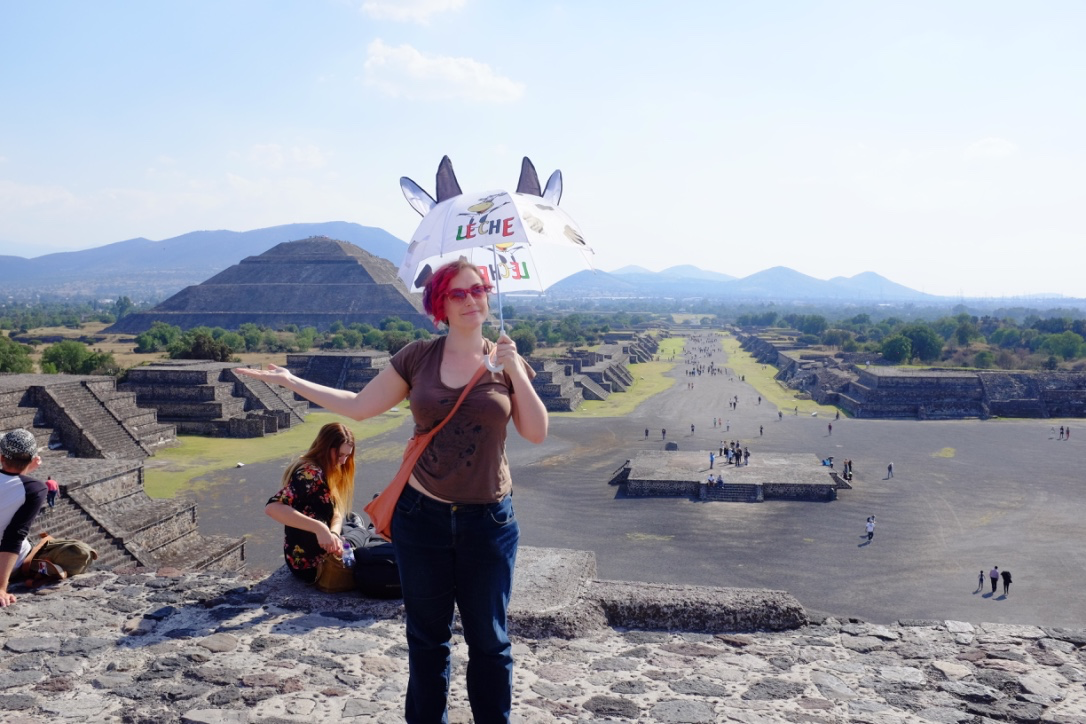Breanne holds an umbrella with cow ears and horns in front of the pyramids of Teotihuacan